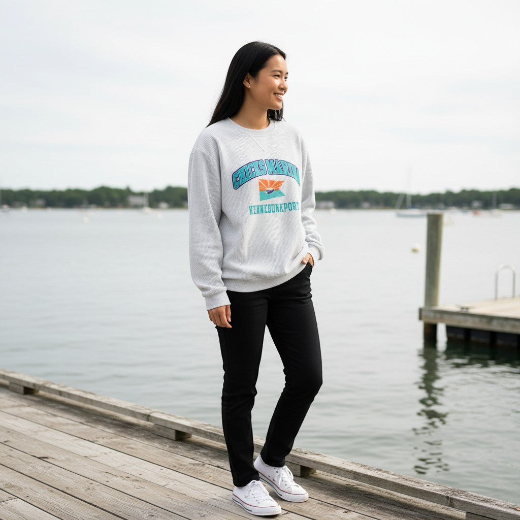 Chicks Marina light grey corduroy crewneck sweatshirt with graphic print on chest, worn by a woman standing on a dock.