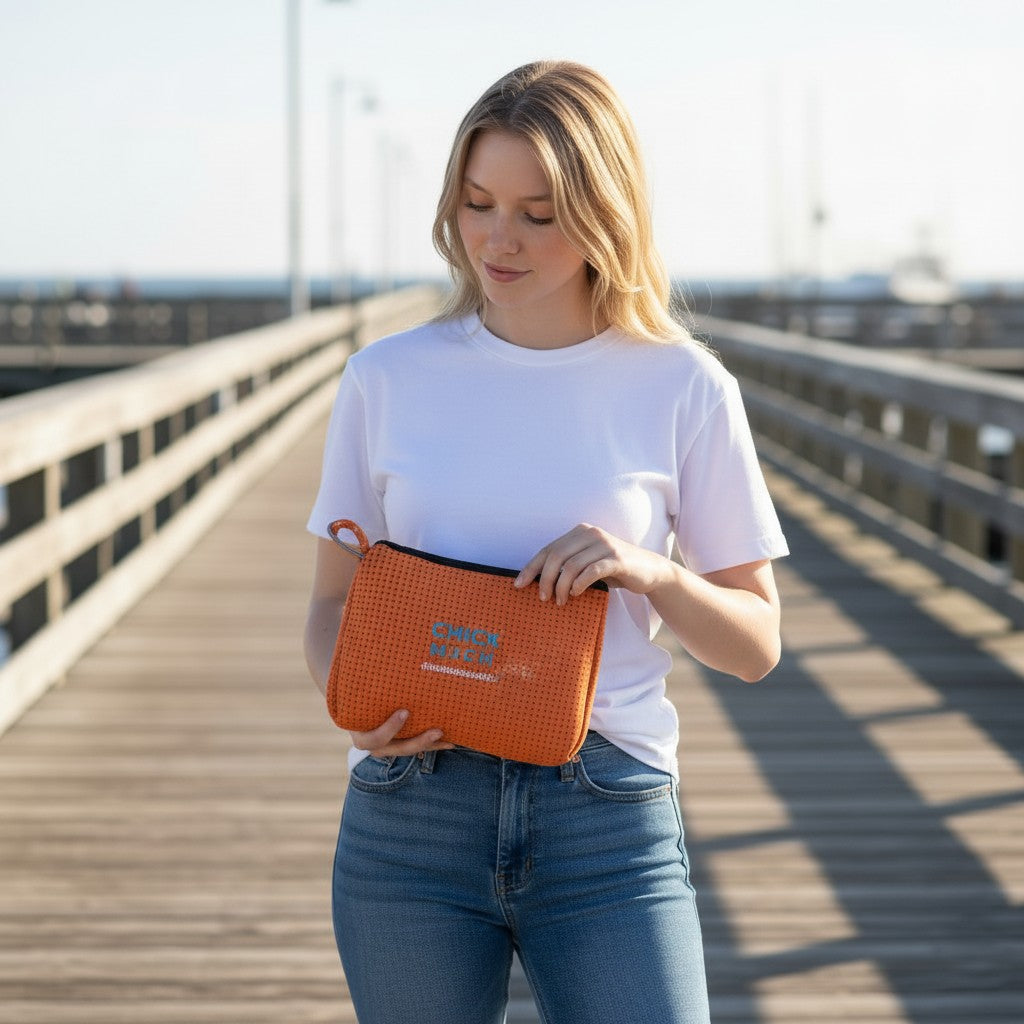 Woman holding an orange Chicks Marina pop pouch with zipper on a wooden pier, featuring a breathable mesh design.