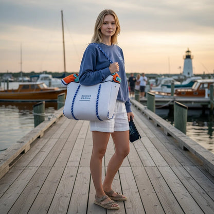 Woman on a marina dock carrying a white perforated Chicks Marina neoprene tote bag with blue rope handles.