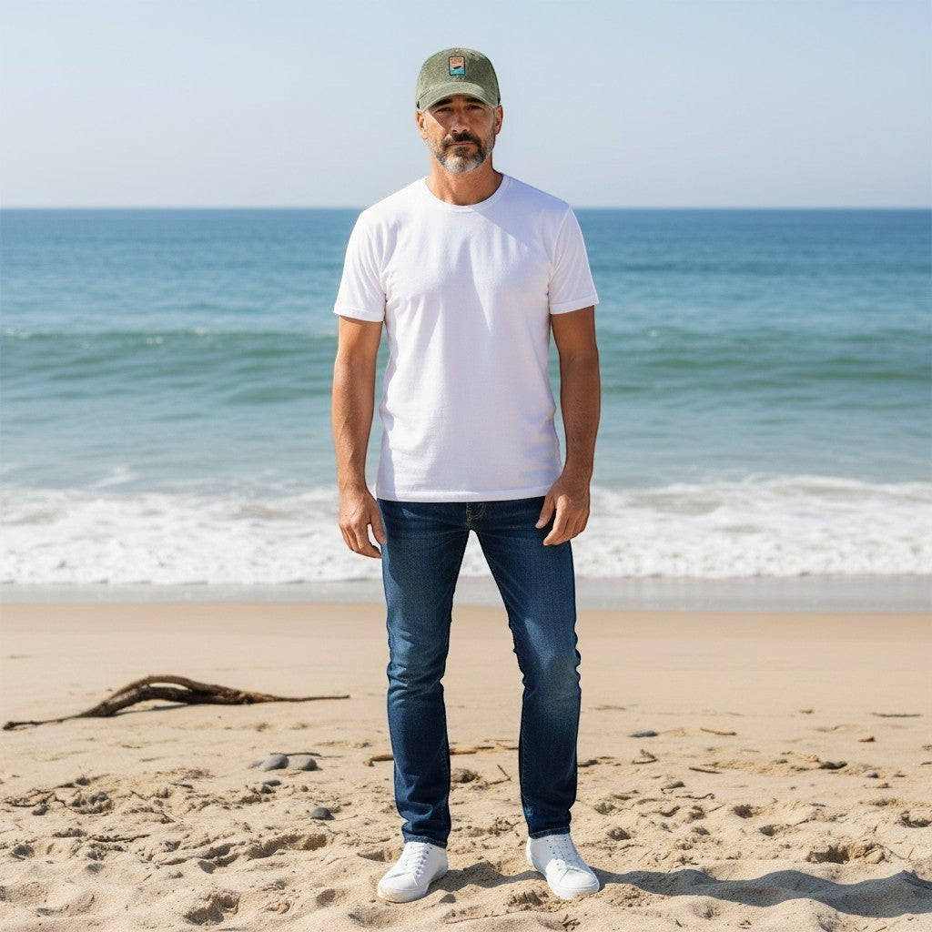 Man wearing a Chicks Marina salt wash corduroy cap with a patch logo, white t-shirt, and jeans on a sunny beach.